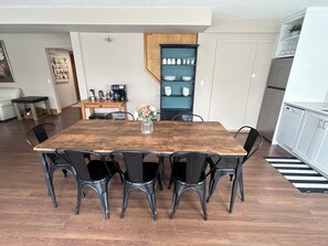 Ein Essbereich mit Holztisch und schwarzen Stühlen, eine Kaffeestation sowie eine Küche mit weißen Schränken und einem Kühlschrank.