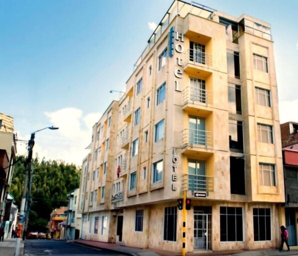 Un hotel de varios pisos con fachada color beige, balcones en los pisos superiores y una entrada visible.