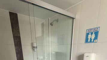 Ett badrum med en dusch som är avskärmad med glasväggar, en toalett och en dispenser för handsprit.
