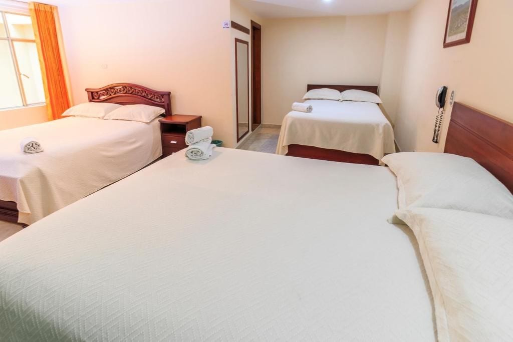 Ein Hotelzimmer mit zwei Einzelbetten, einem hölzernen Kopfteil, einem Nachttisch mit Telefon und einem Fenster mit Vorhängen.