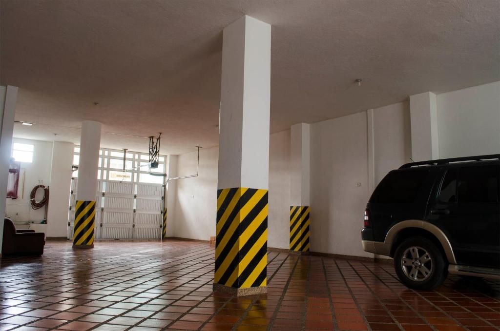Un garaje para coches con suelo de baldosas, pilares blancos y un vehículo negro estacionado a la derecha.