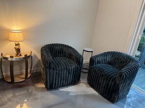 A room with two dark, textured armchairs, a small round table with a lamp, and a view of the outdoors through a window. - Wine Down in Blanco — Two King Master Suites & Hill Country Luxury (Blanco)