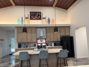 Een moderne keuken met houten kastjes, een centraal eiland met barkrukken, een roestvrijstalen afzuigkap en een zwarte koelkast.