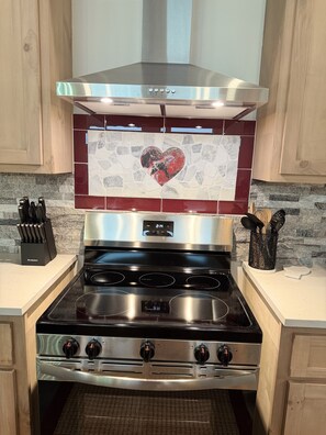 A kitchen with a stainless steel range hood, a heart-shaped tile backsplash, and a black stovetop with four burners. - Wine Down in Blanco — Two King Master Suites & Hill Country Luxury (Blanco)