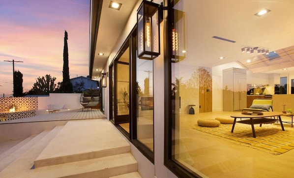 Un interior moderno con una puerta de vidrio que da a un patio, un comedor con mesa y sillas, y una cocina a la vista.