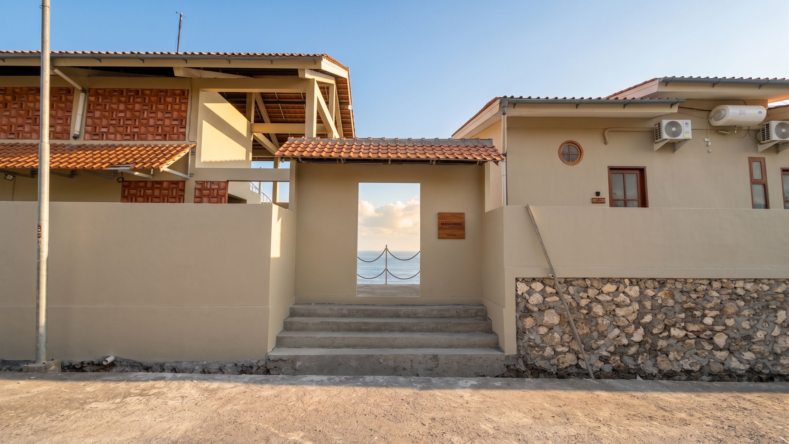 A building with a stone wall, a wooden door, and a view of the sea through a window.