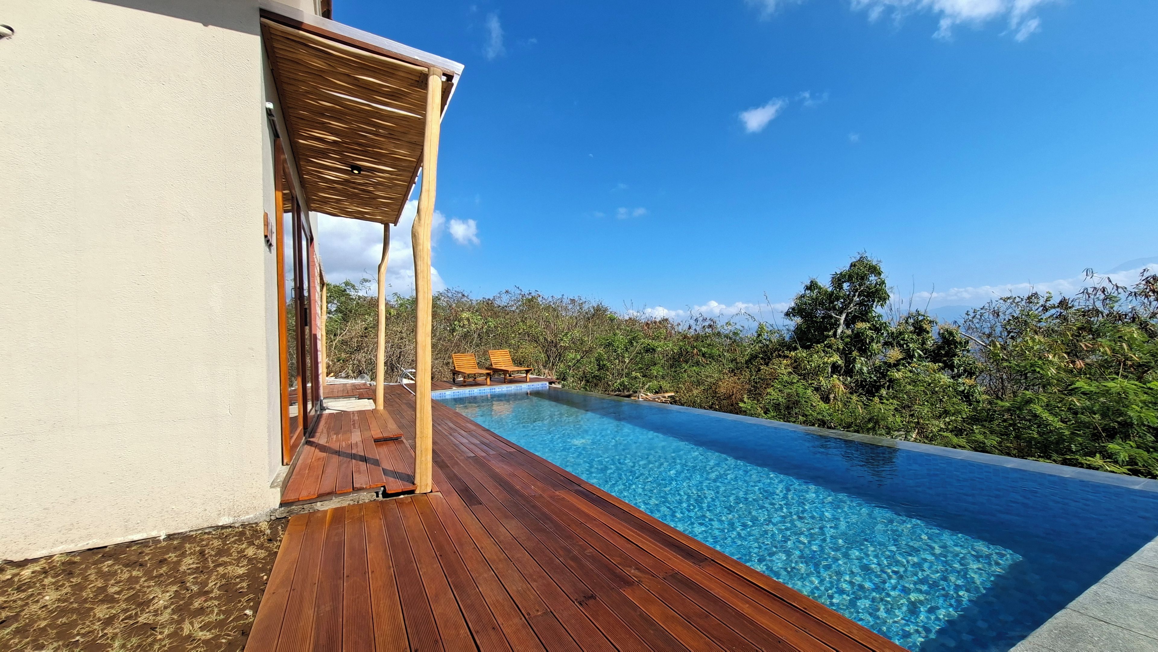 Una terraza de madera que da a una piscina con dos tumbonas y una pérgola.