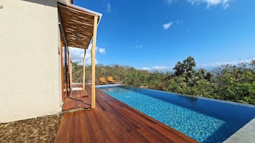 Una terraza de madera que da a una piscina con dos tumbonas y una pérgola.