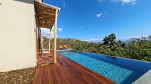 A wooden deck leading to a swimming pool with two lounge chairs and a pergola.