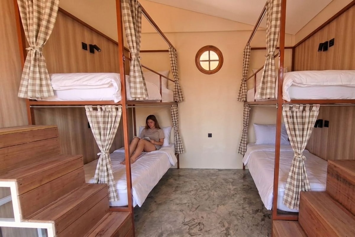 A room with bunk beds, a small window, and a checkered curtain.
