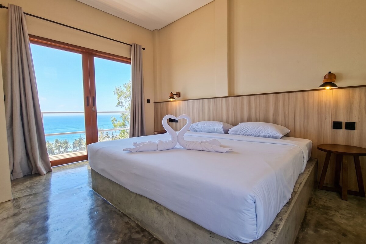 A hotel room with a large bed, a view of the ocean, and a wooden headboard.