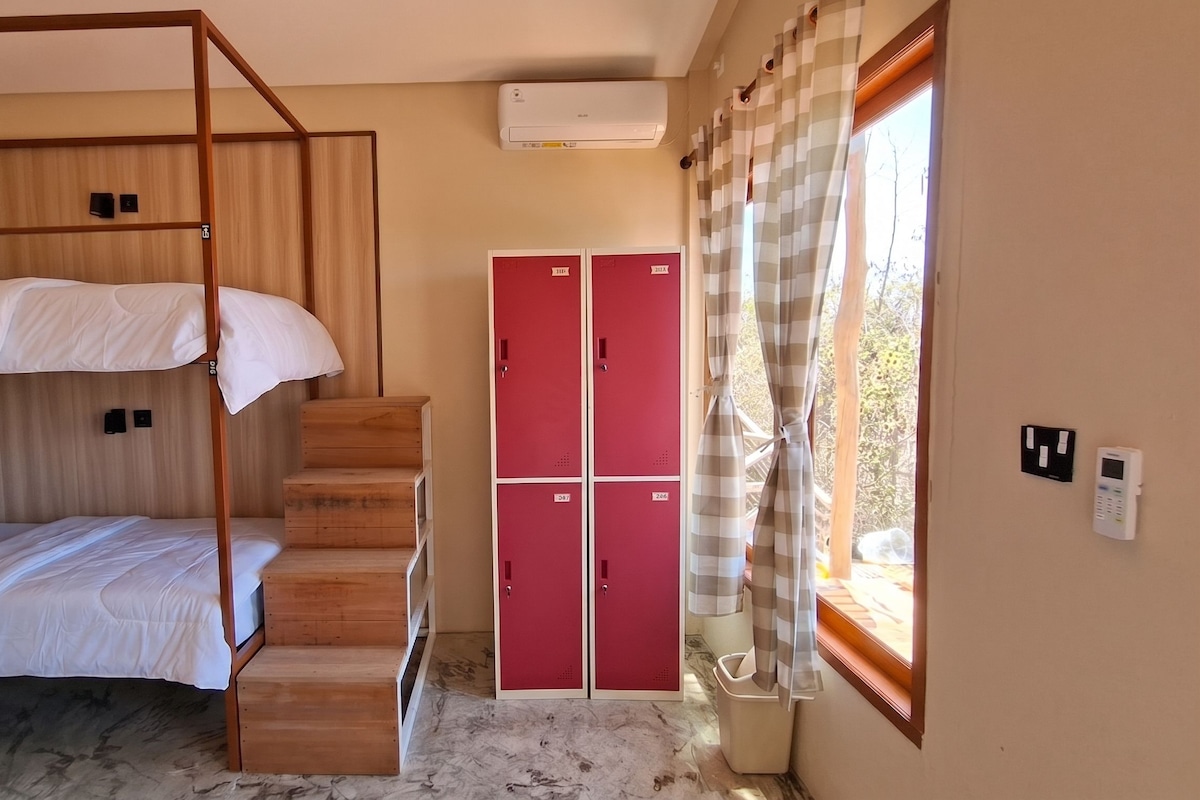 Ein Zimmer mit Etagenbetten, einer Holztreppe, roten Schließfächern und einer Klimaanlage.