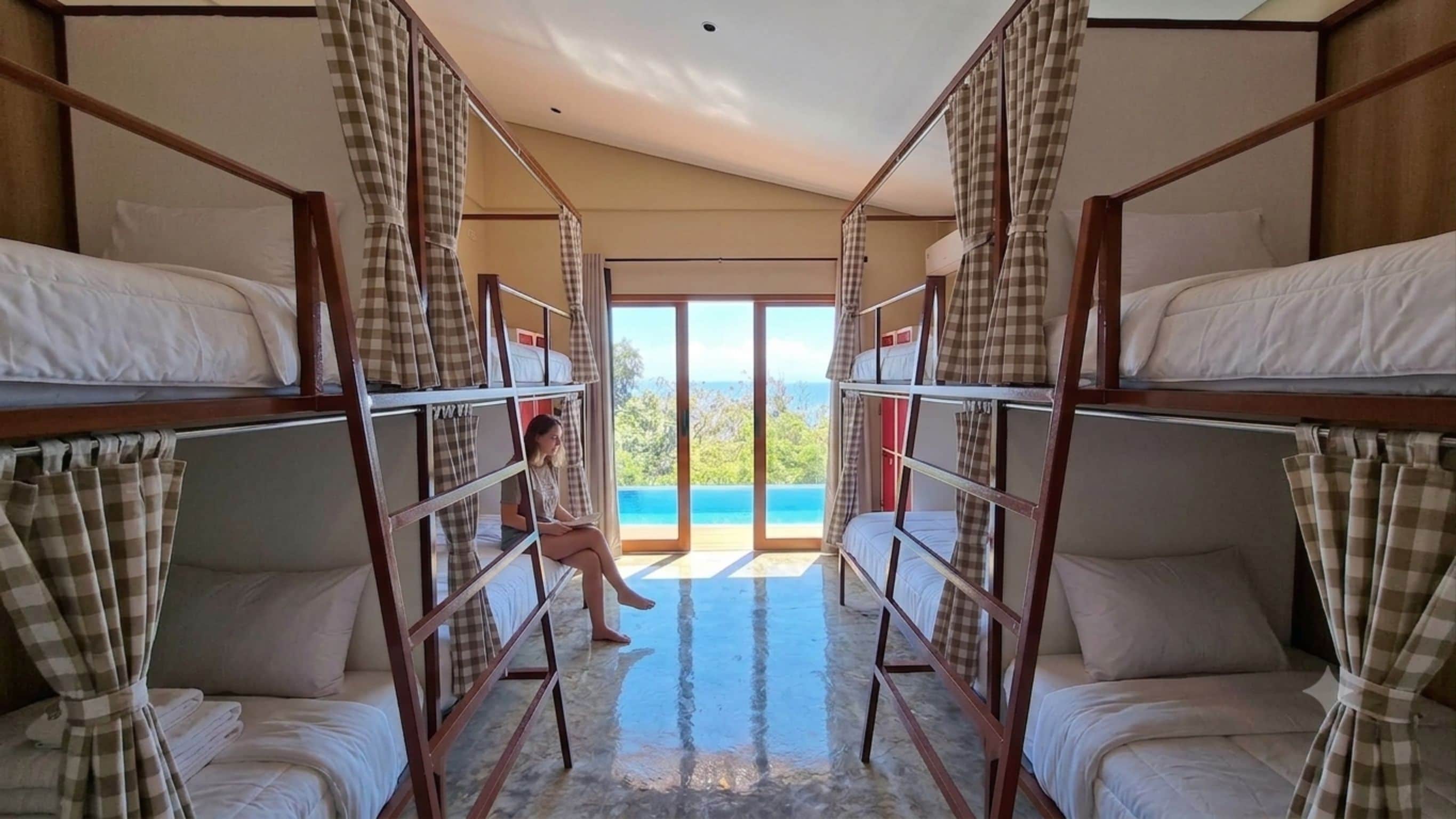 A room with bunk beds, checkered curtains, and a view of a blue body of water.