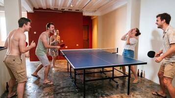 A group of people playing table tennis in a room with a ping pong table, a red wall, and a wooden door.