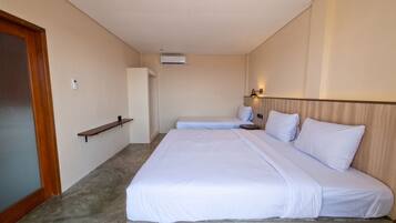 Una habitación de hotel con una cama, una mesita de noche, un estante y un equipo de aire acondicionado.