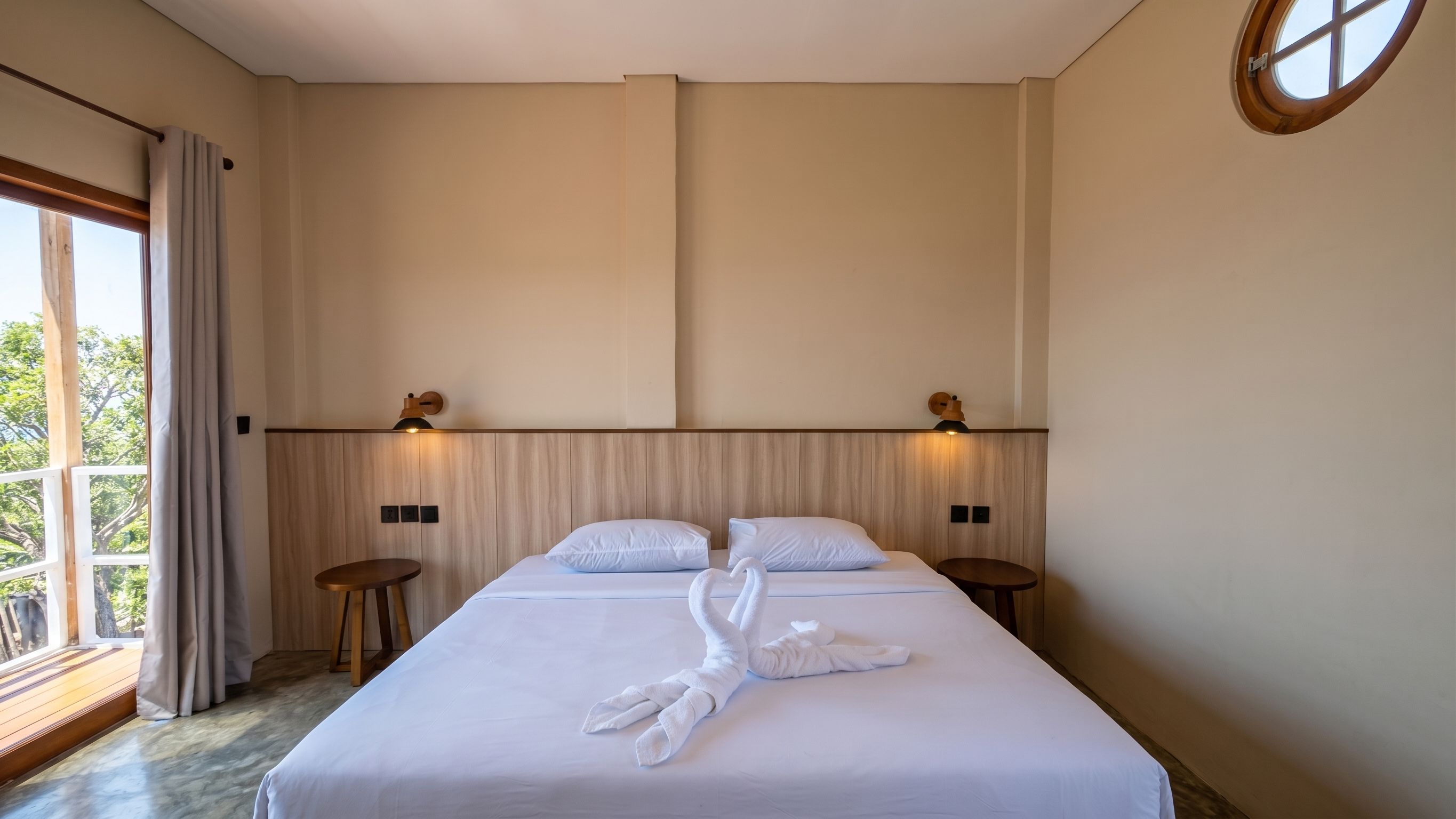 Habitación de hotel con una cama grande, dos mesitas de noche, una ventana con cortinas y vistas a zonas verdes.