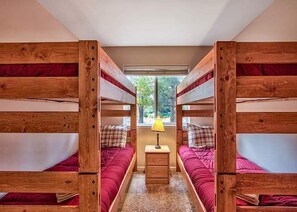 A room with bunk beds, a small bedside table with a lamp, and a window with a view of trees. - Keys Lagoon Retreat (South Lake Tahoe)