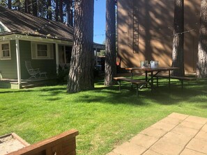 Ein Garten mit einem Picknicktisch, einer kleinen Gartenhütte und zwei großen Bäumen.