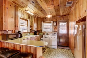 A wooden cabin interior with a kitchen featuring a stove, refrigerator, and bar seating. - Cedar Cabin Lake Tahoe -Walking Distance to Lake (South Lake Tahoe)