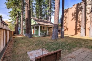 A small wooden cabin with a porch, surrounded by tall trees and a brick wall. - Cedar Cabin Lake Tahoe -Walking Distance to Lake (South Lake Tahoe)