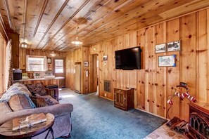 Ein gemütliches Blockhaus-Interieur mit Holzvertäfelung, einem an der Wand befestigten Fernseher und einem Kamin.