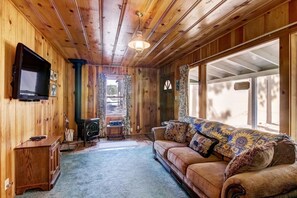A cozy room with a wooden interior, a sofa with patterned cushions, a television mounted on the wall, and a window providing natural light. - Cedar Cabin Lake Tahoe -Walking Distance to Lake (South Lake Tahoe)
