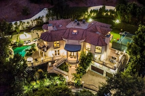 Ein großes, mehrgeschossiges Haus mit Swimmingpool, Sitzgelegenheiten im Freien und gut beleuchteter Fassade.