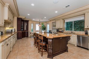 A spacious kitchen with a large island, dark wood cabinetry, and a view of greenery outside. - Mediterranean Beverly Hills estate w/pool, spa & fire pit, sleeps 14 (Beverly Hills)
