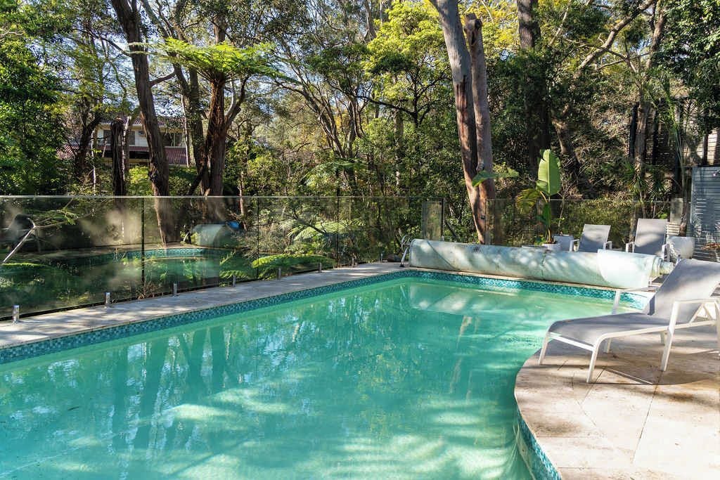 A swimming pool with a tiled edge, surrounded by trees and a fence.
