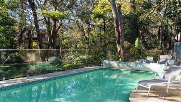 Una piscina con borde de azulejos, rodeada de árboles y una valla.