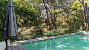 Una piscina con borde de azulejos, rodeada por una valla y árboles.
