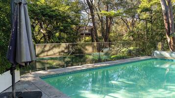 A swimming pool with a tiled edge, surrounded by a fence and trees.