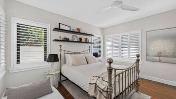 A bedroom with a bed, a nightstand, a lamp, a window with blinds, a ceiling fan, and a bookshelf.