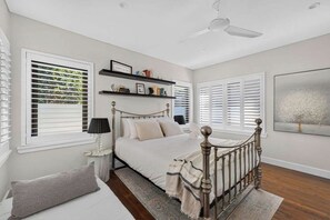 A bedroom with a bed, a nightstand, a lamp, a window with blinds, a ceiling fan, and a bookshelf. - Elegant Lane Cove Sanctuary (Lane Cove)