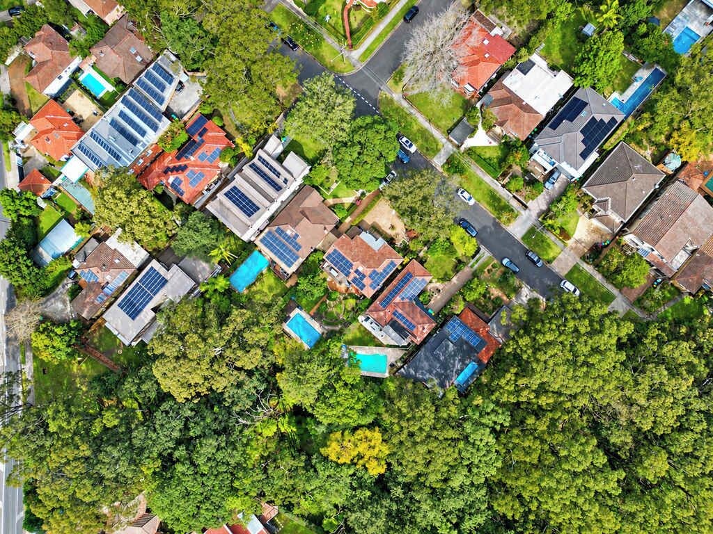 An aerial view of a residential area with houses, solar panels, and green spaces.