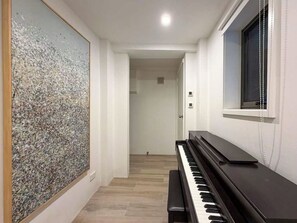 Un pasillo con un piano, un cuadro abstracto de gran tamaño y una puerta que da a otra habitación.