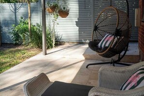 Un patio con mobiliario de mimbre, una silla colgante y plantas en macetas.