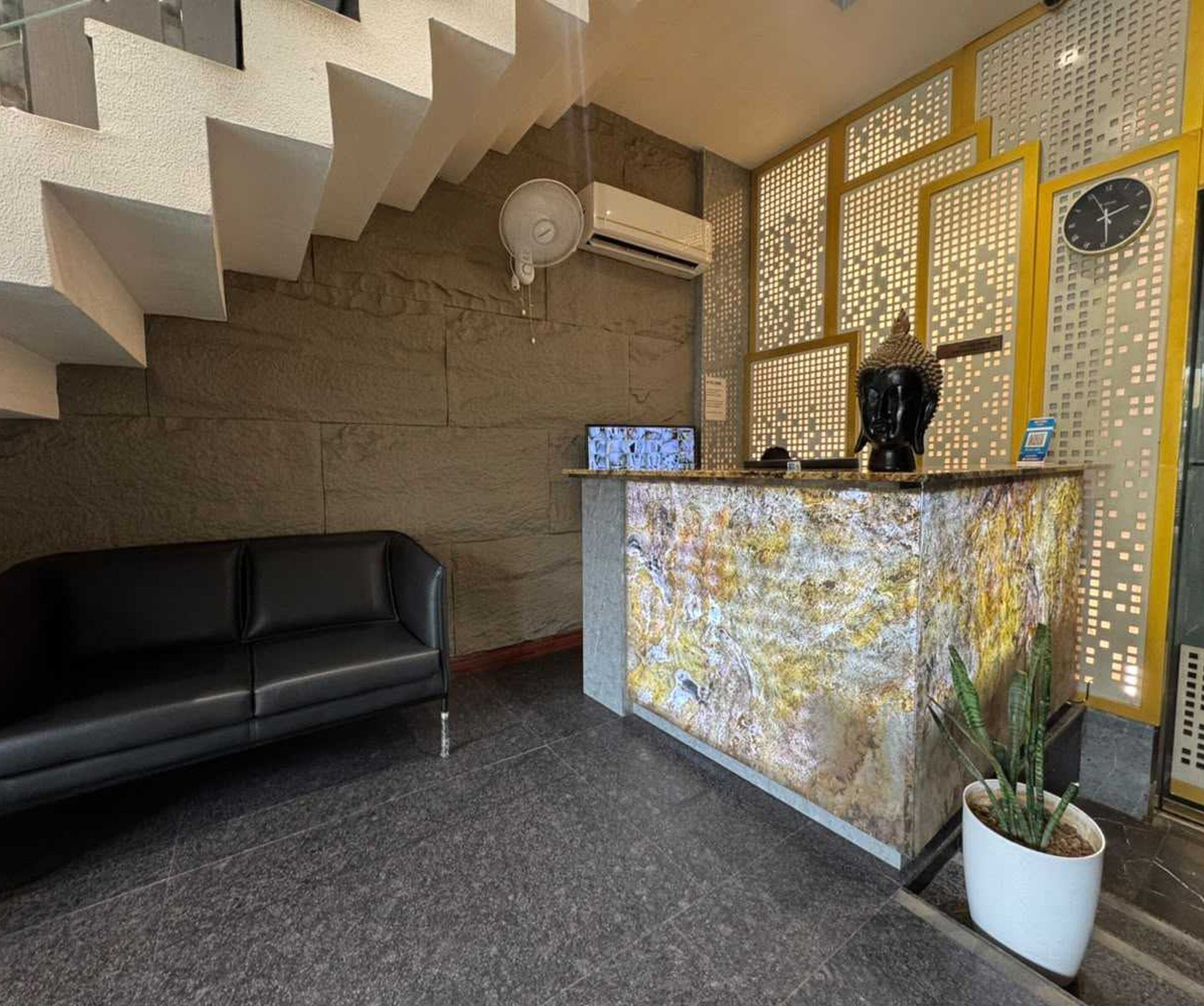Ett väntrum med en svart lädersoffa, en receptionsdisk i marmor, en Buddha-staty och en klocka på väggen.