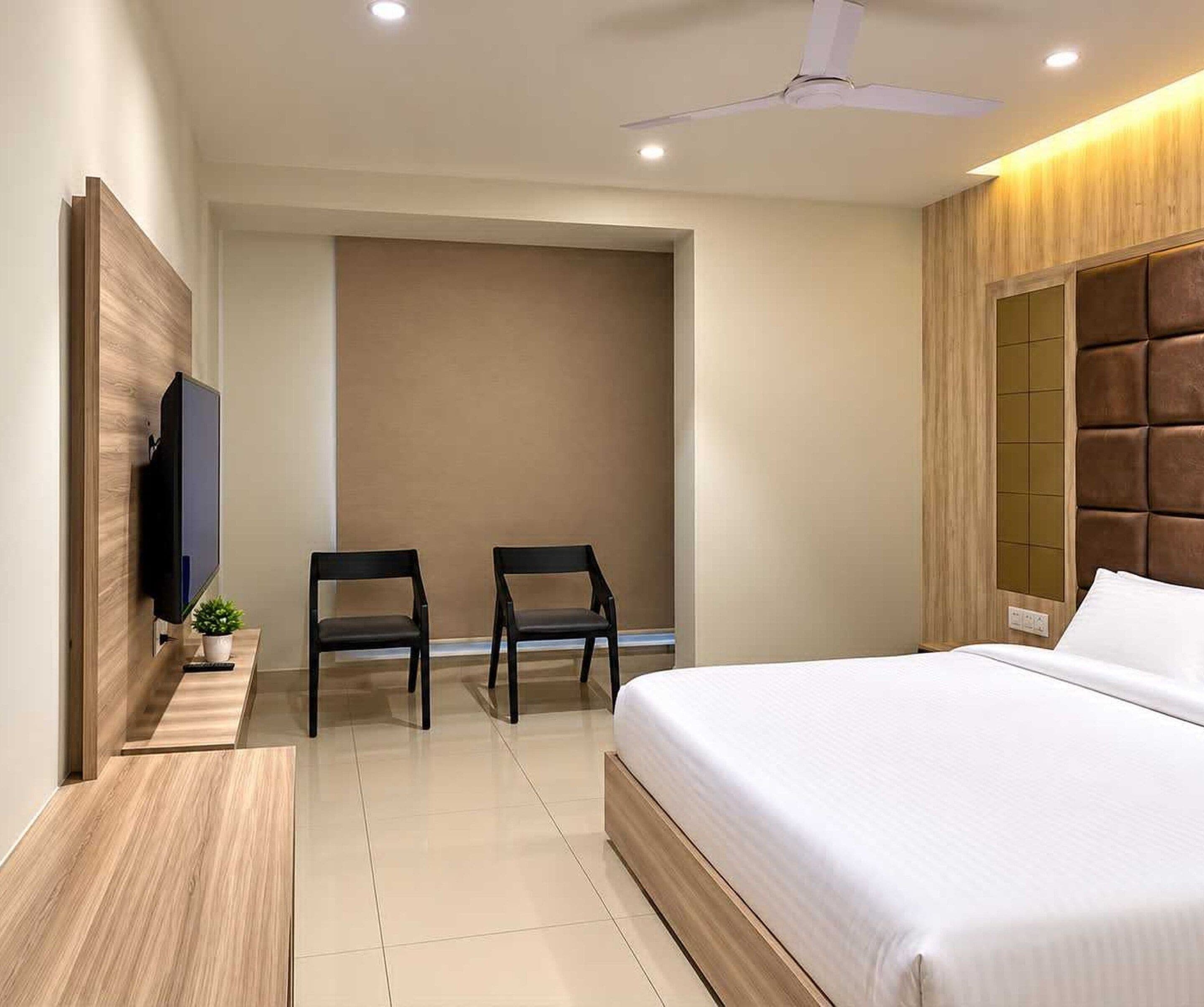 Un dormitorio moderno con una cama, dos sillas, un televisor y un ventilador de techo.