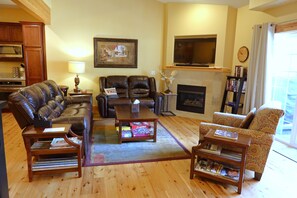 A living room with a fireplace, leather sofas, a coffee table, and a television. - Downtown Leavenworth 2BR/2BA condo with fireplace, deck, parking. (Leavenworth)