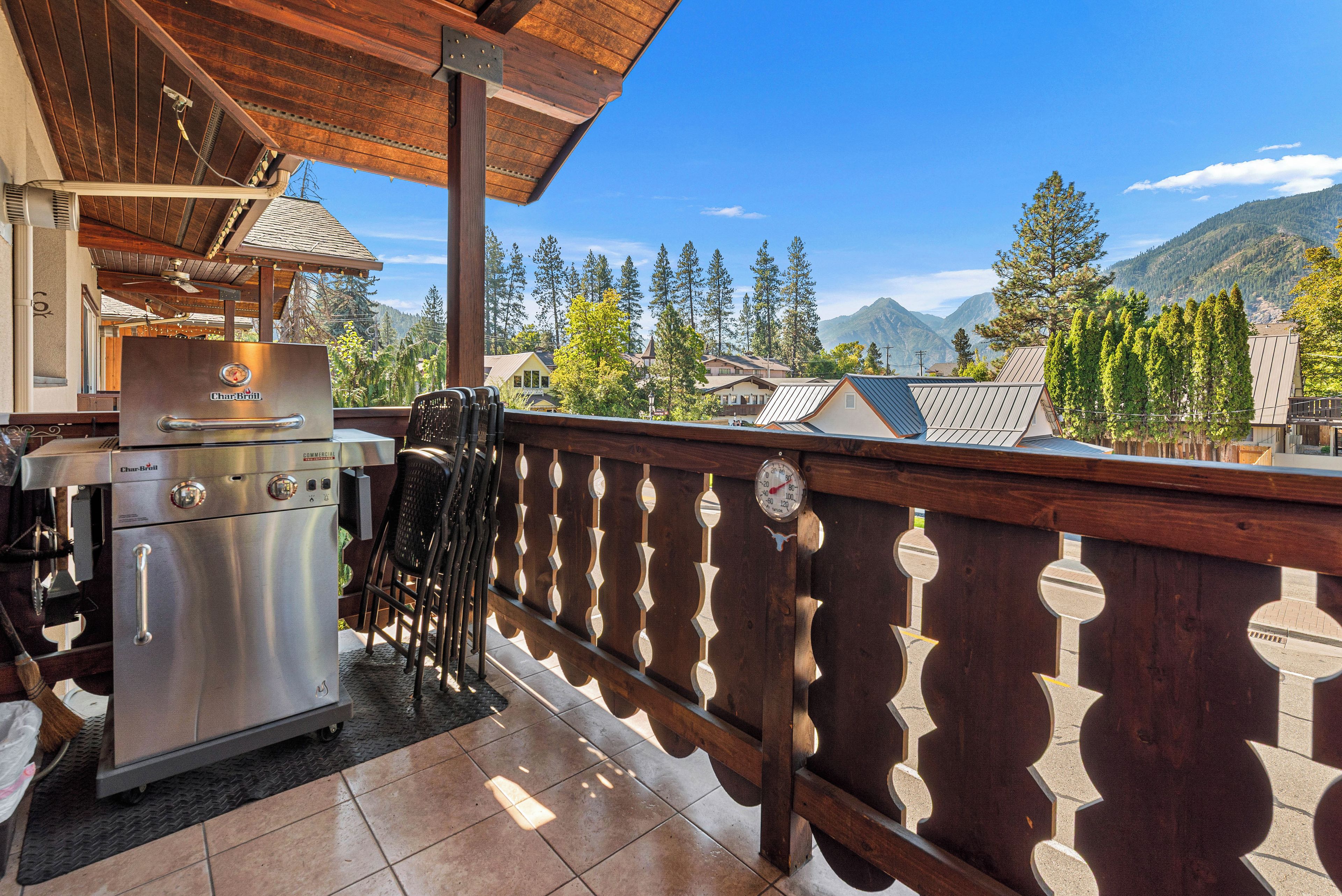 An outdoor kitchen area with a Char-Broil grill, a bar stool, and a wooden railing overlooking a mountainous landscape.