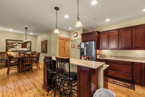 A spacious kitchen with wooden cabinets, a central island with bar stools, a refrigerator, and pendant lighting. - Downtown Leavenworth 2BR/2BA condo with fireplace, deck, parking. (Leavenworth)