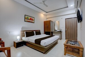Ein Hotelzimmer mit Bett, Nachttisch, Schrank, Fernseher und einem Gemälde an der Wand.