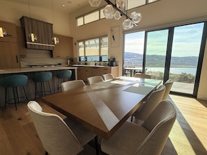 A modern kitchen with a large island, bar stools, and a dining area with a long table and chairs. - Luxury Skyridge home - sleeps 12 - large game room (Daniel)