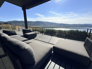 A deck with a sofa and ottoman, overlooking a lake and mountains. - Luxury Skyridge home - sleeps 12 - large game room (Daniel)