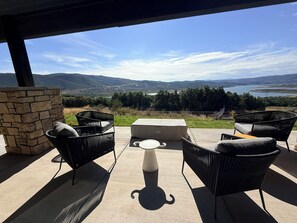 Eine Terrassensitzgruppe im Freien mit Korbmöbeln und einer Steinmauer, mit Blick auf eine malerische Landschaft mit Hügeln und einem Gewässer.