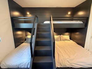 Ein Schlafraum mit Stockbett, einer zentralen Treppe, weißer Bettwäsche und Wandleuchten.