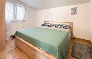 Ein Einzelzimmer mit einem hölzernen Kopfteil, einer grünen Tagesdecke und zwei gemusterten Kissen.