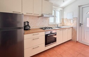 Eine kompakte Küche mit Kühlschrank, Herd, Backofen und Kaffeemaschine.