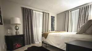 Una habitación de hotel con cama, mesita de noche, lámpara, alfombra y cortinas.